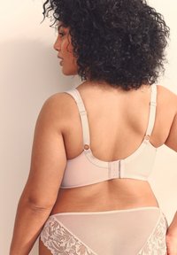 Beige bh med justerbare stropper og hægte-lukning med øje, med en glat tekstur. Blondefront på matchende trusser tilføjer detalje.