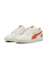 Biele kožené tenisky s oranžovým pruhom. Majú okrúhlu špičku, perforované detaily a textúrovanú gumovú podrážku. Logo PUMA na jazyku.