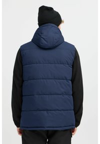Marineblauer Puffweste mit Kapuze, die horizontale Nähte und eine glatte Textur aufweist, getragen über einem schwarzen Langarmshirt.