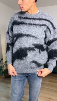 Grijze gebreide trui met zwarte abstracte patronen. Gemaakt van zacht, gestructureerd materiaal, met een ronde hals en een relaxte pasvorm.