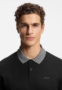 Czarna koszulka polo z fakturowanym szarym kołnierzem. Posiada dwukolorowy kołnierz zapinany na dwa guziki oraz dyskretne logo "BOSS" na piersi. Gładka faktura materiału.