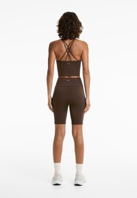 Brown athletic cropped top with multiple crossover straps, paired with matching bike shorts, both made from smooth, stretchy fabric.