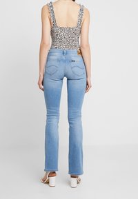 Body de estampado de leopardo con tirantes volantes, combinado con jeans acampanados azul claros, que presentan un parche de logo en la parte trasera y suturas sutiles.