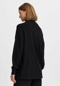 Pulover negru supradimensionat cu guler înalt, mâneci lungi și deschideri laterale, realizat dintr-un material moale. Textură netedă și croi lejer.