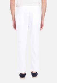 Pantaloni bianchi in lino, dal taglio dritto, con tasche posteriori e vita a media altezza, abbinati a scarpe navy.