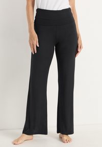 Zwarte flared broek met een brede tailleband, gemaakt van zachte stof. Het ontwerp heeft zijsplitten aan de zoom, wat zorgt voor meer bewegingsvrijheid.