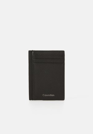  Porte-cartes en cuir noir avec une surface texturée, comprenant plusieurs emplacements pour cartes et un logo argenté en bas. Design rectangulaire compact.