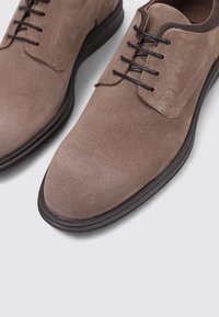 Zapatos derby de ante marrón con un acabado suave, punta redondeada, diseño de cordones de seis ojales y una suela de goma oscura contrastante.