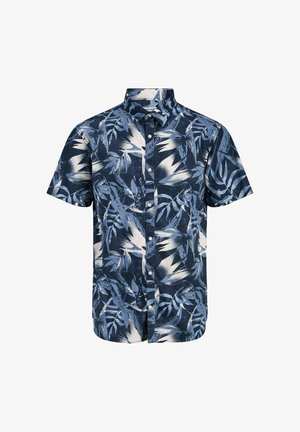 Ragazzo con camicia a maniche corte a motivi di foglie bianche e blu, pantaloncini blu navy, calzini bianchi e scarpe beige, in piedi e che guarda verso sinistra.