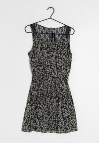 Robe fleurie à fond noir, ornée de motifs de marguerites blanches, sans manches, avec des détails en dentelle au niveau du col et une taille élastique.