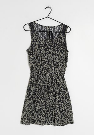 Robe fleurie à fond noir, ornée de motifs de marguerites blanches, sans manches, avec des détails en dentelle au niveau du col et une taille élastique.