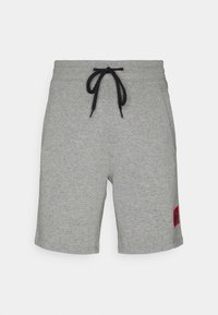 Shorts en coton gris avec une taille à cordon de serrage, arborant un patch logo rouge sur la jambe gauche et une coupe décontractée, droite.