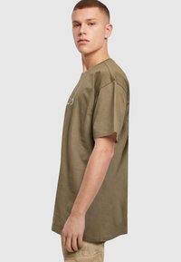 Oliven grøn bomulds T-shirt med korte ærmer, afslappet pasform og et lille rundt logo foran. Glat tekstur, regular afslutning.