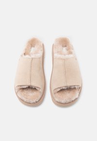 Μπεζ παντόφλες με ανοιχτά δάχτυλα, με μαλακή, αφράτη επένδυση, σουέτ εξωτερικό και μαξιλαρωμένες σόλες, τοποθετημένες δίπλα-δίπλα σε λευκό φόντο.