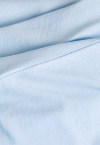 Svetle modrá tkanina s jemnou texturou, která má hladký povrch a decentní horizontální žebrování. Viditelné vrstvy zavěšené a složené.