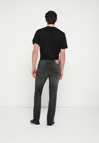 Čierne tričko v kombinácii s tmavo modrými, úzkymi džínsami. Džínsy majú zadné vrecká a malú značkovú štítok na opasku. Celý look dopĺňajú tenisky.