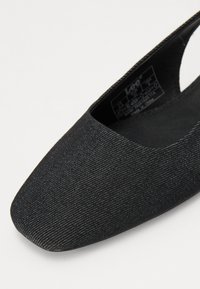 Sapato slip-on de tecido preto com bico quadrado e textura lisa. O interior apresenta um acolchoamento mínimo, com uma etiqueta visível no interior.