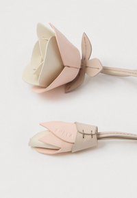 Rózsaszín és krémszínű bőr virág alakú tárgy, réteges szirmokkal és varrással díszített szárával. "FURIA" felirattal jelölve.