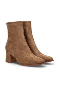 Botas de ante marrón hasta el tobillo con punta afilada y tacón cuadrado. Presenta un acabado suave y costuras visibles a lo largo del borde superior. Suela plana.