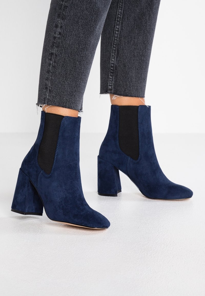Bottines en daim bleu marine avec bout pointu et talon bloc, dotées de panneaux latéraux élastiques et d'une finition texturée lisse.