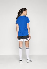 Blue athletic shirt with short sleeves, black shorts featuring white stripes, and knee-high white socks with black bands and footwear.