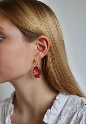 Goldfarbene Ohrringe mit einem großen, facettierten, tropfenförmigen roten Edelstein. Das Design beinhaltet kleine Metallakzente und einen einfachen Hakenverschluss.