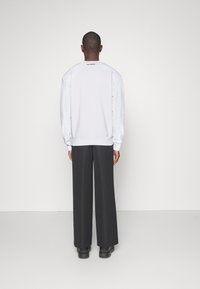 Sudadera blanca de manga larga, con puños acanalados y cuello redondo, combinada con pantalones negros de pierna ancha y calzado oscuro.