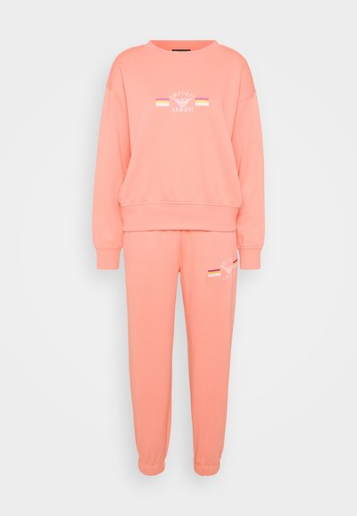 Sweatshirt rose clair et joggings assortis en tissu doux. Présente une broderie avec un logo. Le sweatshirt a un col rond et des poignets côtelés.