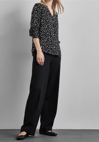 Svartvit mönstrad blus med v-ringning, långa ärmar och uppvikta manschetter, ihopparad med svarta vida byxor och platta skor.