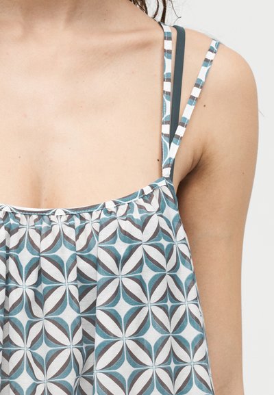 Κοντινό πλάνο τοπ χωρίς μανίκια με διπλές τιράντες και γεωμετρικό μοτίβο σε χρωματισμούς τιρκουάζ, γκρι και λευκό στο άνω μέρος του στήθους και τον ώμο μιας γυναίκας.