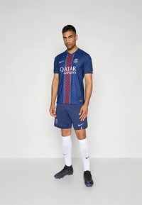 Plavi nogometni dres s crvenim uzorkom duž središta, s logotipom "Qatar Airways". Uparen s tamnoplavim hlačama i bijelim čarapama. Crne kopačke.