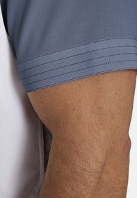 Kurzarmshirt aus grauem strukturiertem Stoff mit drei horizontalen Streifen nahe dem Ärmel, kontrastiert mit einem weißen Körper.