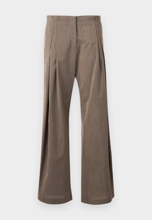 Femme portant un haut blanc sans manches, un pantalon large marron taille haute, des sandales noires à talons et des colliers dorés superposés.