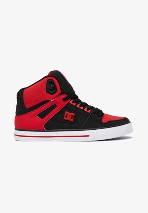 Zapatilla de caña alta negra y roja con suela blanca, logo rojo de DC en el lateral, cordones negros y collarín acolchado rojo y negro para el tobillo.
