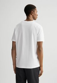 Witte katoenen t-shirt met korte mouwen en een ronde hals, met een eenvoudige uitstraling en een relaxte pasvorm, weergegeven van de achterkant.