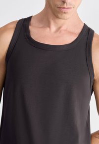 Débardeur gris foncé avec un col rond, sans manches, et une texture lisse avec un col renforcé.