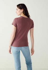 Kortærmet, tætsiddende T-shirt i dæmpet rosa, med rund halsudskæring og ribbet struktur, parret med lyseblå jeans.