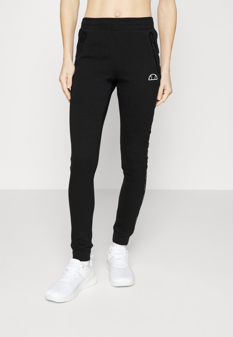 Schwarze Stretch-Jogginghosen mit schmaler Passform, ausgestattet mit seitlichen Taschen mit Reißverschluss und einem Logo-Detail an der linken Hüfte. Weiche, glatte Textur.