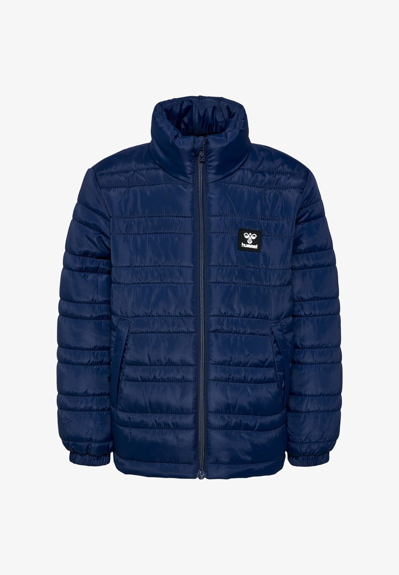 Marineblå pufferjakke med vertikale syninger, høj krave, frontlynlås og sidelommer. Har et sort logo-patch på venstre bryst.