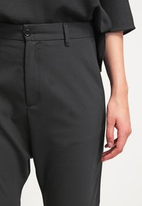 Šedé kalhoty na míru s hladkou texturou, s jedním knoflíkem, bočními kapsami a rovnými nohavicemi.