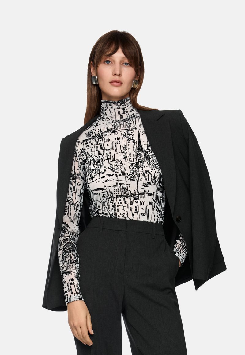 Schwarz-weiß gemusterter Rollkragenpullover mit einem Stadtbilddesign, kombiniert mit einem dunkelgrauen Blazer und maßgeschneiderten Hosen. Glatte Stofftextur.