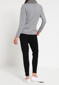 Grijze trui met geribde kraag, gecombineerd met zwarte slim-fit broek en witte sneakers. Voorzien van een logopatch op de linkerschouder.