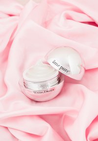 Round, silver jar of "Wrinkle Eraser" cream with a white lid, containing smooth, off-white cream, resting on soft pink fabric.
