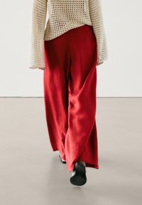 Pantalon fluide en lin rouge taille haute, à la texture douce, associé à un haut à manches longues en maille de couleur crème.