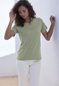 Light green cotton t-shirt with a round neckline, short sleeves, and a small "Copenhagen" logo printed on the front. Worn with white pants.