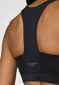 Μαύρο αθλητικό στηθόδεσμο με κομψό σχέδιο, πλέγμα στα πλάγια και λεπτομέρεια με λογότυπο στο πίσω μέρος κάτω από την τιράντα.