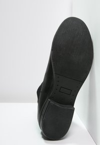 Scarpa nera con suola in gomma testurizzata, dotata di punta tondeggiante e materiale superiore liscio. Progettata per comfort e stabilità.