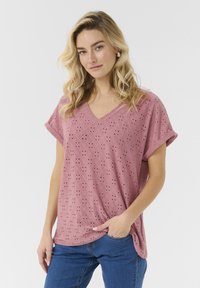 Haut rose à manches courtes avec un col en V, orné d'un motif d'œillets et d'une coupe décontractée. Texture douce et poignets de manches roulés.