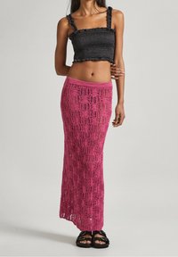 Top corto nero con arricciature e spalline a volant abbinato a una lunga gonna rosa in cotone lavorato all'uncinetto con un motivo aperto e una cintura elastica.