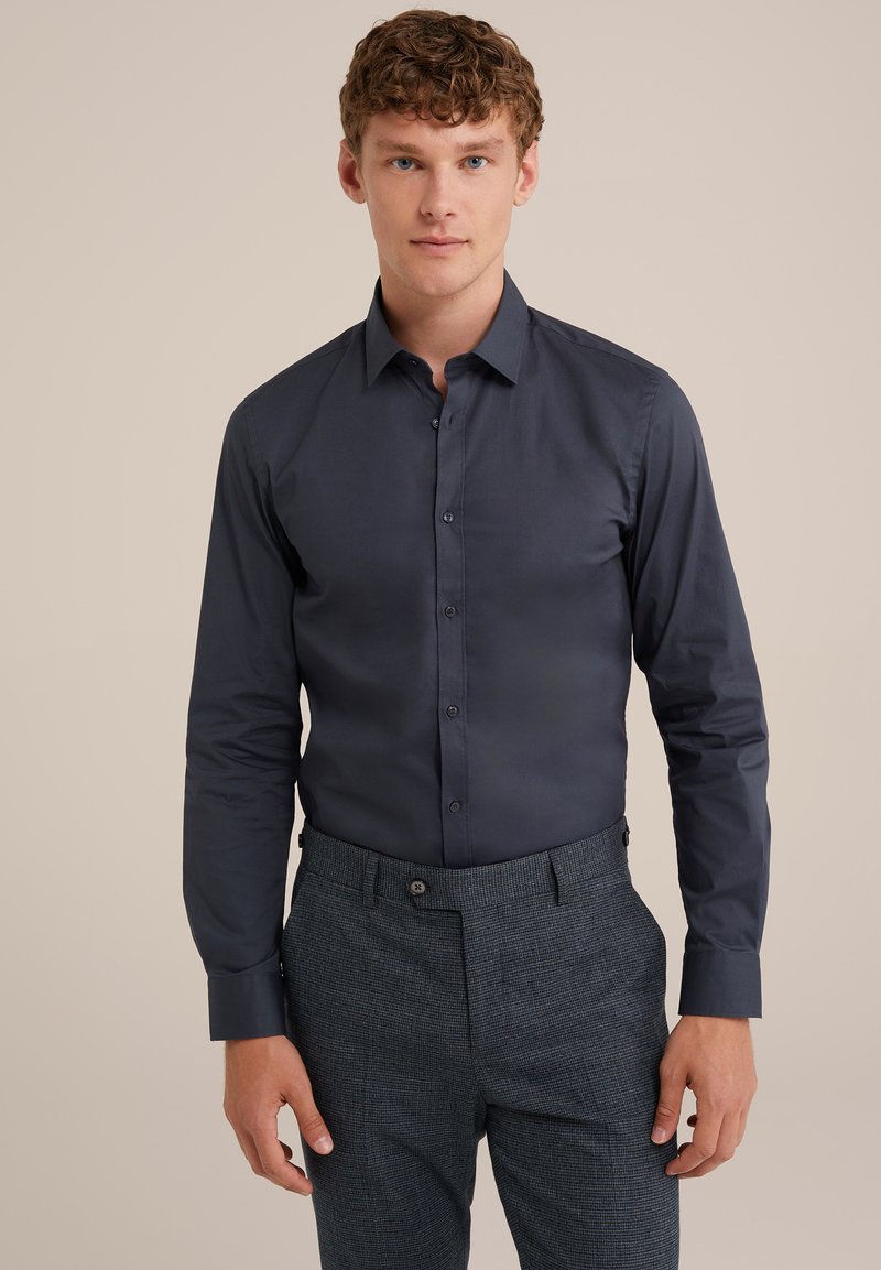 Camisa de manga larga azul oscuro con un corte ajustado, diseño de botones en el frente y textura suave, combinada con pantalones grises con patrón y un ajuste entallado.